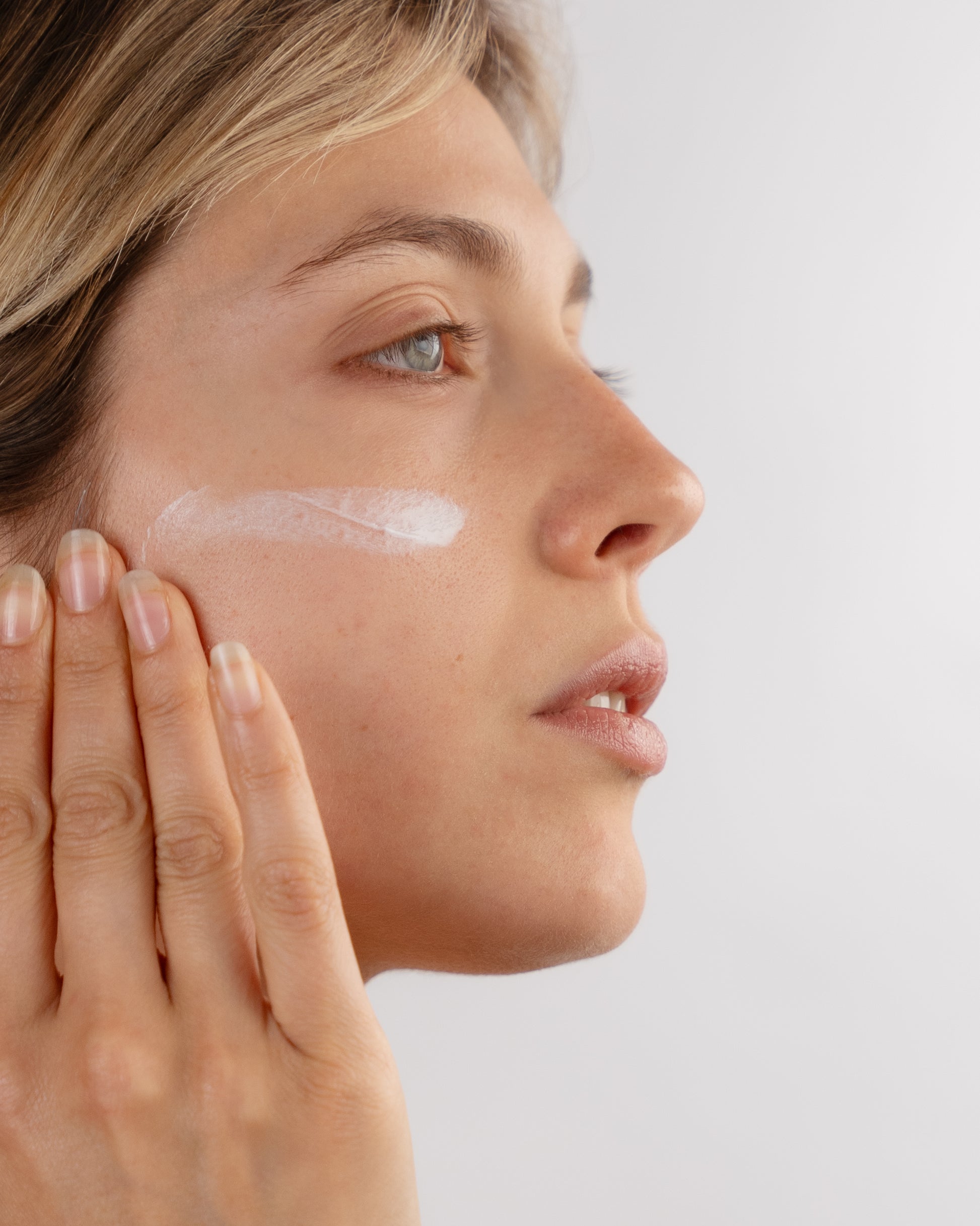 Foto di una giovane donna che applica The Intensive, la crema viso antirughe e nutriente di DF18+. 